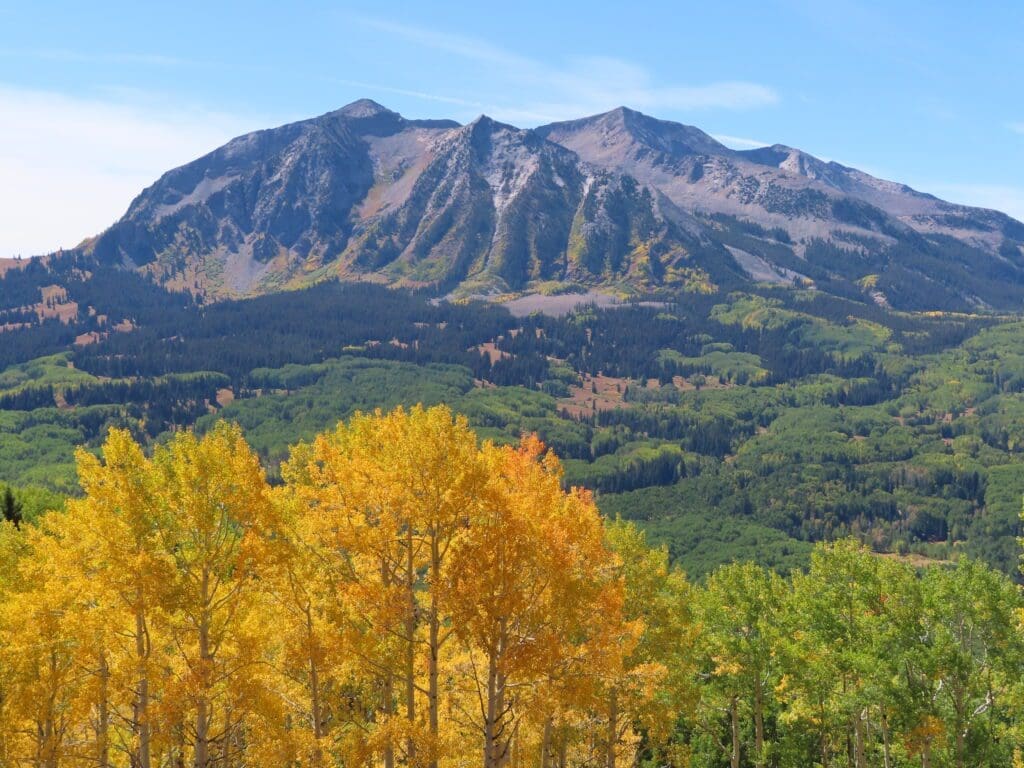 A mountain with trees in the foreground and some mountains behind it.