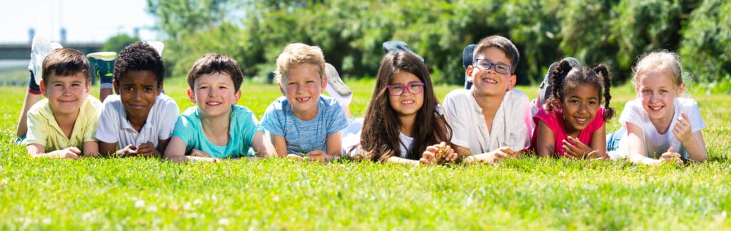 Happy,Children,Lie,On,The,Green,Grass,On,A,Sunny