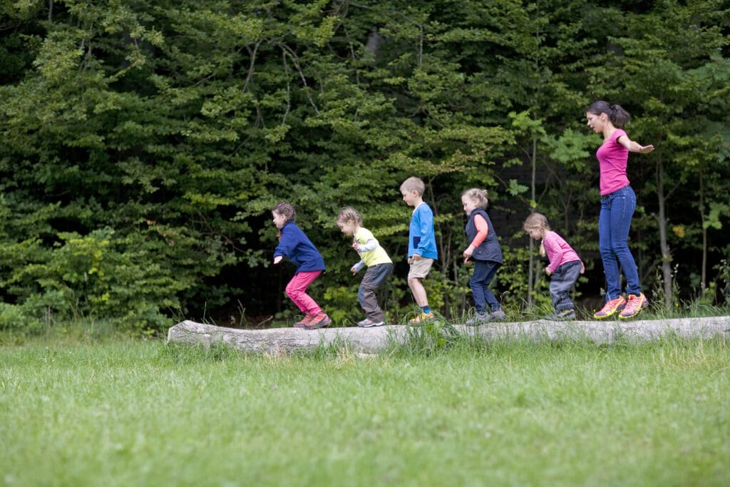 Kindergarten,Teacher,Playing,With,Kids,On,Log,In,A,Wood